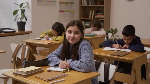Smiling Girl Looking at Camera at Desk in School Classroom