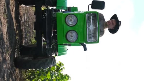 A Handsome Farmer is Driving a Tractor Black and Red Currant Bushes Grow in Rows on the Plantation