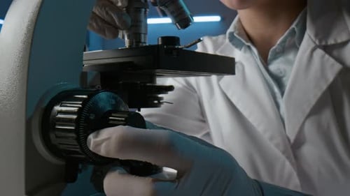 Unknown Scientist Wearing White Coat and Sterile Gloves Working with Microscope