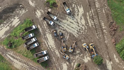 Aerial View of Construction Site with Heavy Machinery and Dump Trucks Working in a Muddy Landscape