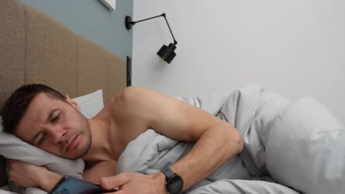 Man Lying in Bed Looking at Smartphone