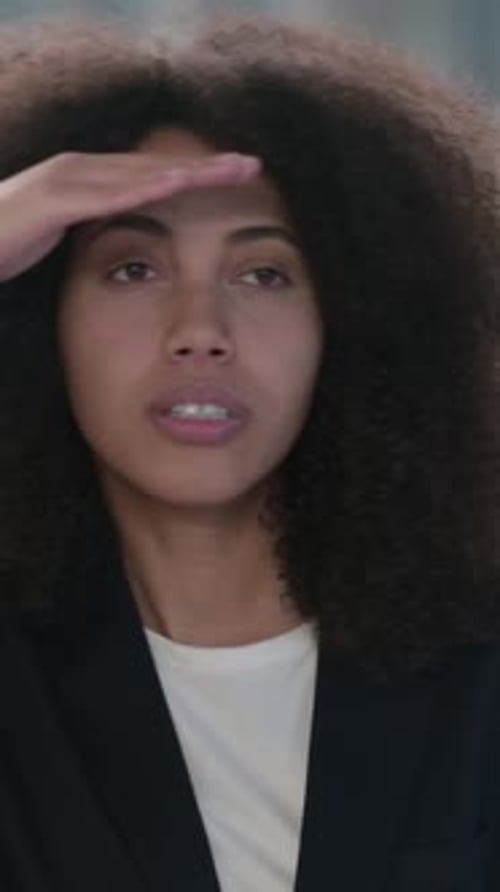 Woman in Blazer Shields Eyes, Looks Up and Smiles