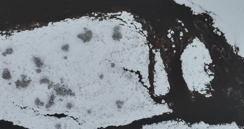 Eine Luftaufnahme eines gefrorenen Flusses, der durch schneebedeckte Wälder fließt, an einem bewölkten Sonnenuntergangshimmel