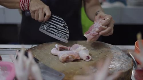 Hände einer Metzgerfrau entknochen Hähnchenschenkel mit einem großen scharfen Messer auf einem großen Holz