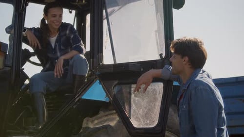 Young Female Farmer in Tractor Cabin Chatting with Man on Farm Field