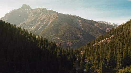 Drohnenflug über dem Bergwald mit Panoramaberg im Hintergrund mit Sonnenstrahl