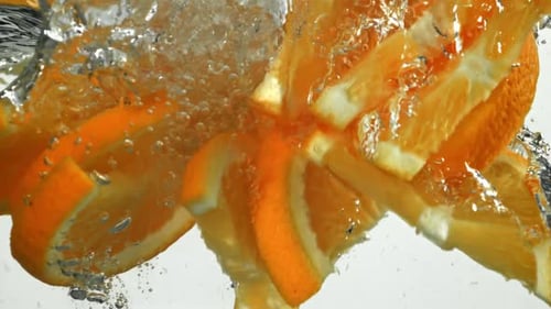 Orangenstücke, die auf weißem Hintergrund unter Wasser fallen, gefilmt mit einer Hochgeschwindigkeitskamera mit 1000 Bildern pro Sekunde