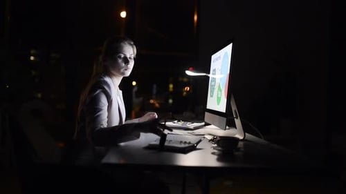 Young businesswoman working late at her computer in a modern office at night