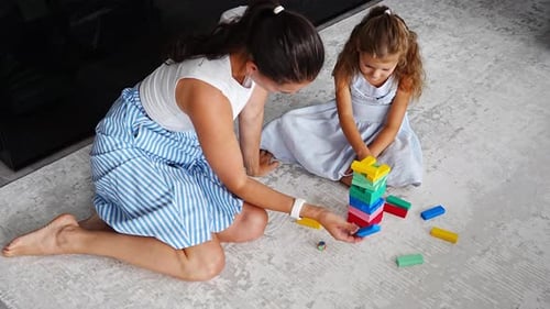 Little Girl with Her Mother Playing Board Game at Home Taking Colorful Blocks From Wooden Tower
