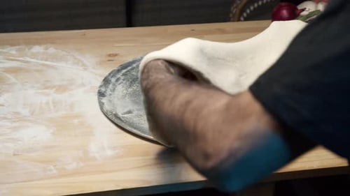 A top-shot of a skilled chef's hands put pizza dough on a steel tray on wooden counter, shallowing i