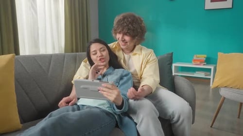A Woman and a Man Watch a Movie on a Tablet Discuss What They Saw A Asian Woman Lies on a Sofa with