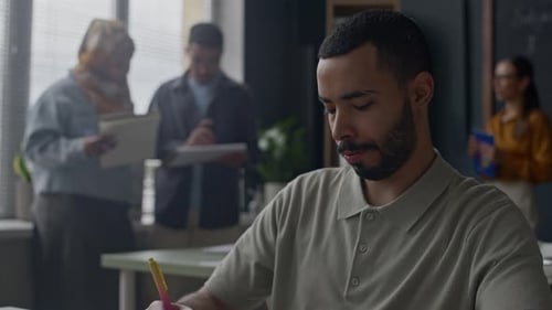 Student Taking Notes at Desk During Classroom Discussion