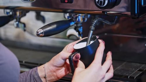 Automatic machine prepares cappuccino. Woman holds the cup near the coffee machine.