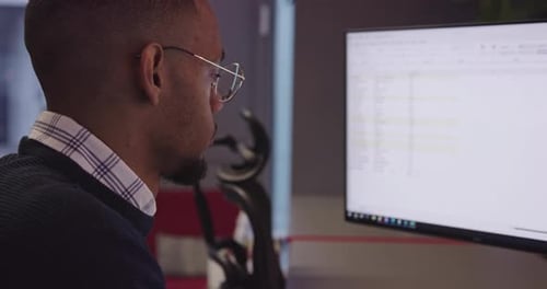 Young African American with Glasses Sitting in a Modern Coworking Office and Working at a Computer