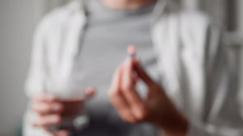 Woman Holds Pill Capsule and Glass of Water