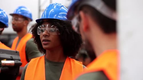 Multi ethnic engineers wearing safety glasses and hardhats working together in a robotics factory, d