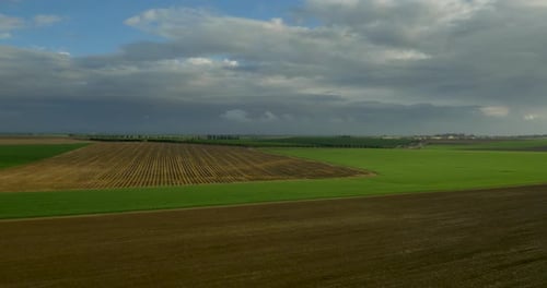 Luftaufnahme von landwirtschaftlichen Feldern mit bewölktem Himmel und Sonne, die sich im Gras spiegelt.