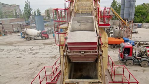 Blick von oben auf einen mit schwarzem Material gefüllten Industrietrichter, umgeben von roten Geländern und Leitern