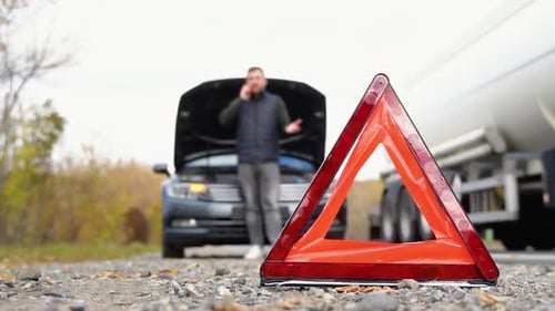 Road Side Warning Triangle Warning Oncoming Traffic of a Broken Down Car with a Man Using His Cell