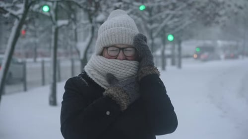 Woman with Glasses Wrapped in Scarf Trying to Hide From Snowfall in City