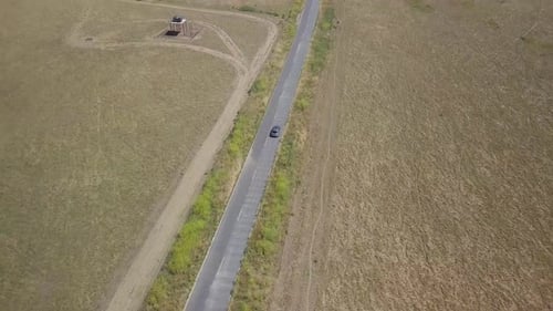 4K Aerial shot of silver SUV driving down long straight country road, isolated against wide open gol