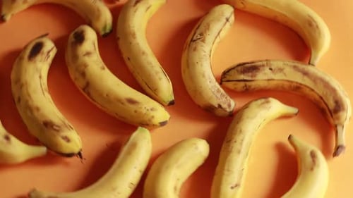 Ripe delicious wet bananas rotate clockwise on a black plate on a yellow background