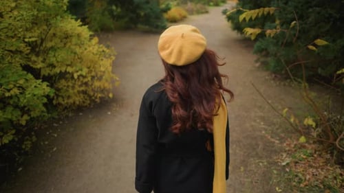 Lady with Yellow Beret Adjusts Hair While Strolling in Garden
