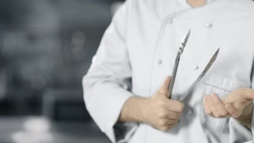 Chef in uniform holding kitchen cooking tongs
