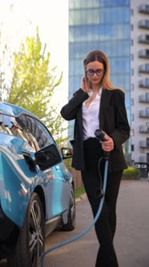 Woman Charging Electric Car in Modern City Highlighting Sustainability and Green Technology