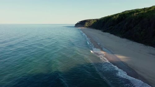 Beach Between a Ledge Covered with Vegetation and a Black Sea Under a Clear Blue Sky