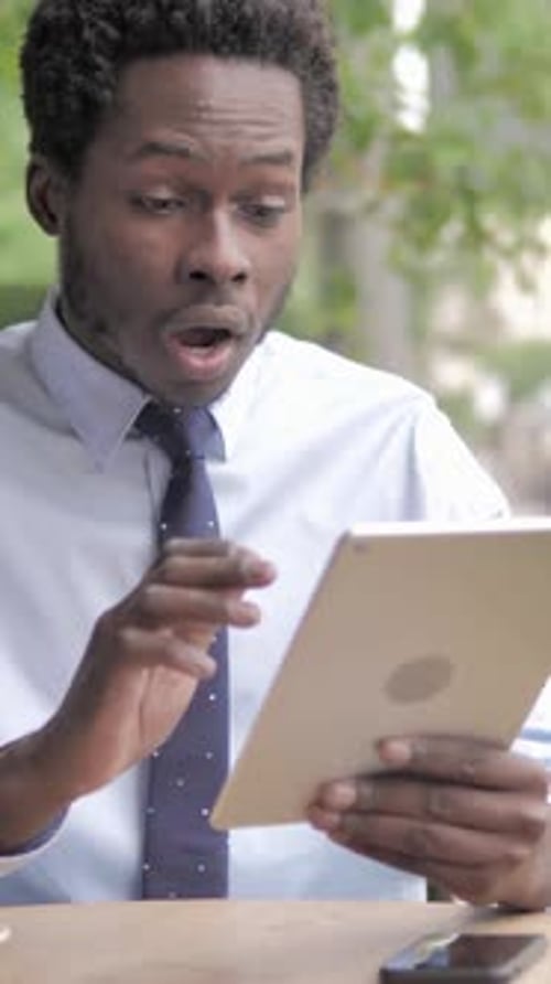 Wow, Shocked African Businessman Using Tablet while Sitting in Outdoor Cafe, Vertical Video