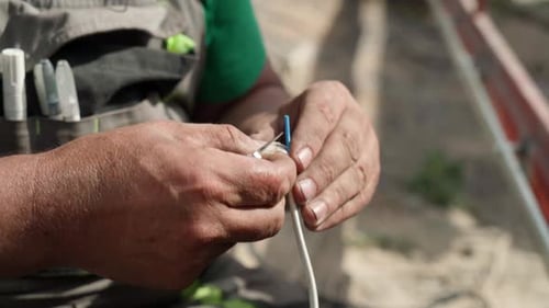 Worker stripping white electric cable with blade