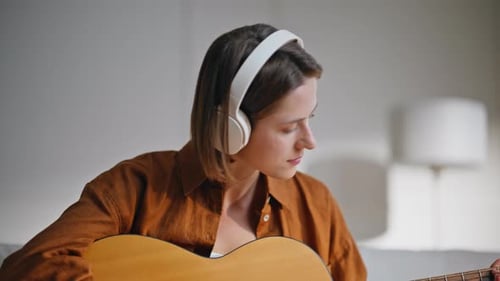 Woman Plays Guitar Wearing Headphones Indoors