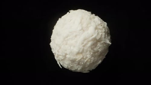 Candy ball with coconut chips. Rotates on a black background, close-up.