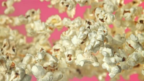Popcorn fliegt hoch und fällt herunter auf einem rosa Hintergrund, gefilmt mit einer Hochgeschwindigkeitskamera mit 1000 Bildern pro Sekunde