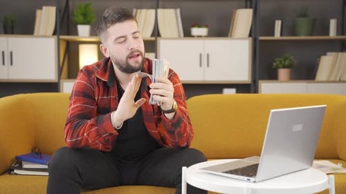 Man Sitting on Couch with Laptop and Money