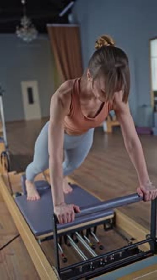 A Woman is Actively Engaging in Pilates on a Reformer Machine at a Fitness Studio Doing Exercises