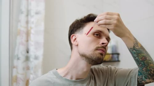 Man Applies Red Serum to Face for Skincare