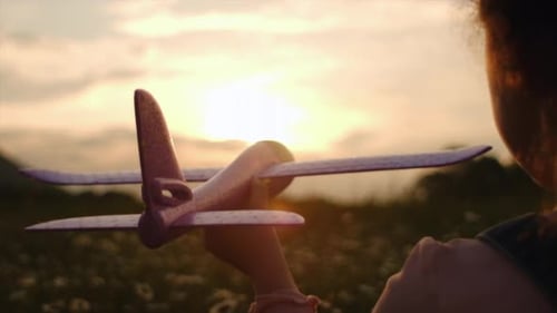 Silhouette of little girl wants to become pilot. Child with toy airplane on field in sunset light