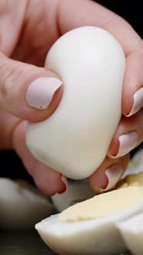 Vertical video. A woman's hand squeezes a boiled egg, causing it to break into small pieces flying
