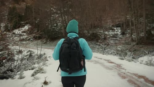 Woman in sportswear with backpack walking along snowy footpath in winter forest