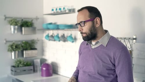 Pensive, Worried Man Drinking Coffee Standing in Kitchen at Home 30s
