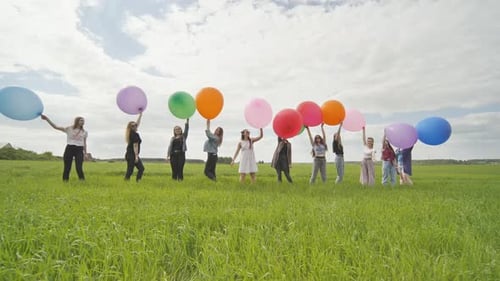 Cheerful Girls are Standing on the Field with Large Balloons and Colorful Balloons