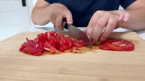 Femme coupant des tomates mûres sur une planche à découper en bois dans une cuisine lumineuse préparant des ingrédients pour