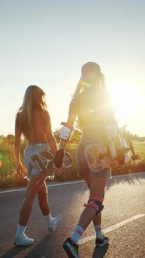 Sporty Women Walk on Country Road at Sunset Carrying Surfskates