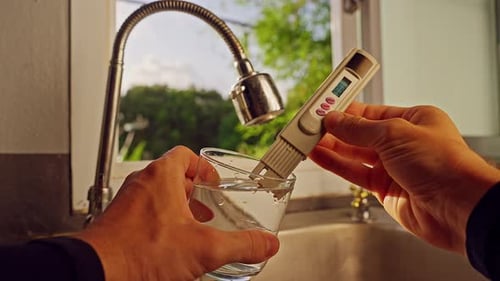 Vue à la première personne des mains mesurant l'eau potable avec un testeur de qualité numérique en verre transparent à proximité