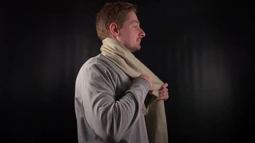 Man Tying Beige Scarf Around Neck, Black Background