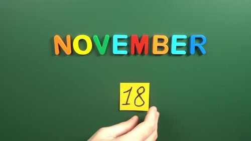 Hand sticking a sticker 18 November calendar day on school board. 18 date of November. Eighteenth