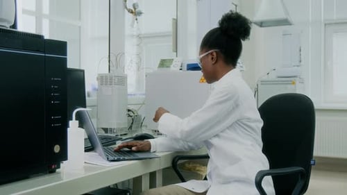 Chemist Typing on Laptop, Then Shaking Content of Test Tube in Laboratory