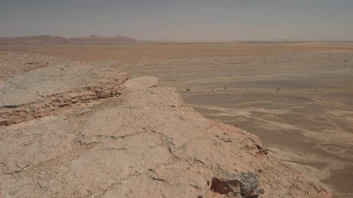 Rocky cliff edge of Gara Medouar overlooking circular erosion patterns on desert floor Morocco